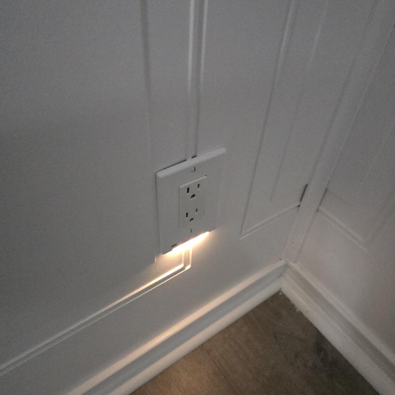 Wall outlet with embedded lighting on a white paneled wall.