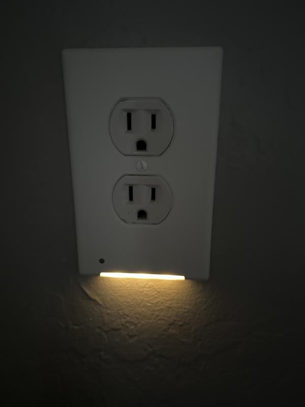 White electrical outlet with a small light illuminated on a dark background